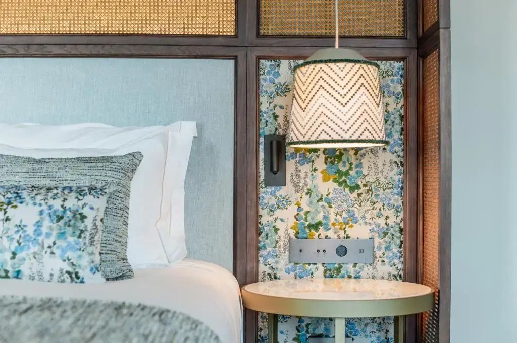 Stilvolle Nachttischlampe und kunstvolle Tapete neben dem Hotelbett