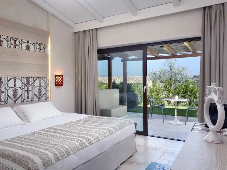 Helles Schlafzimmer mit Doppelbett und Zugang zu einer Terrasse mit Gartenblick