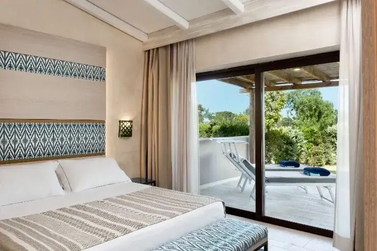 Helles Schlafzimmer in der Suite mit Gartenblick im Baglioni Resort Sardinia mit Zugang zur Terrasse.