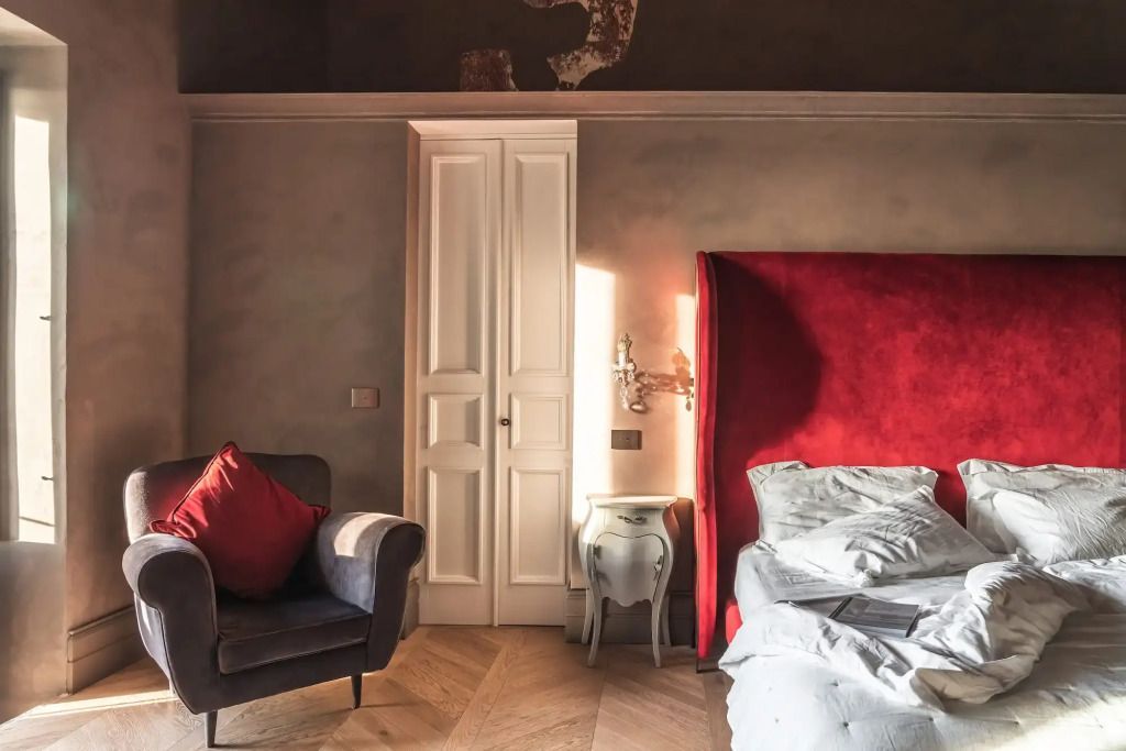 Elegantes Hotelzimmer mit rotem Samtkopfteil, gepolstertem Sessel und weißer Tür.