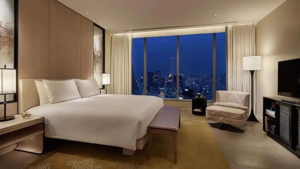 Luxuriöses Schlafzimmer in einer Suite mit Blick auf die erleuchtete Stadt bei Nacht.