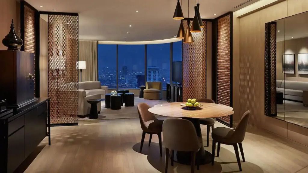 Stilvolles Wohnzimmer einer Suite mit modernen Möbeln und nächtlichem Stadtpanorama.