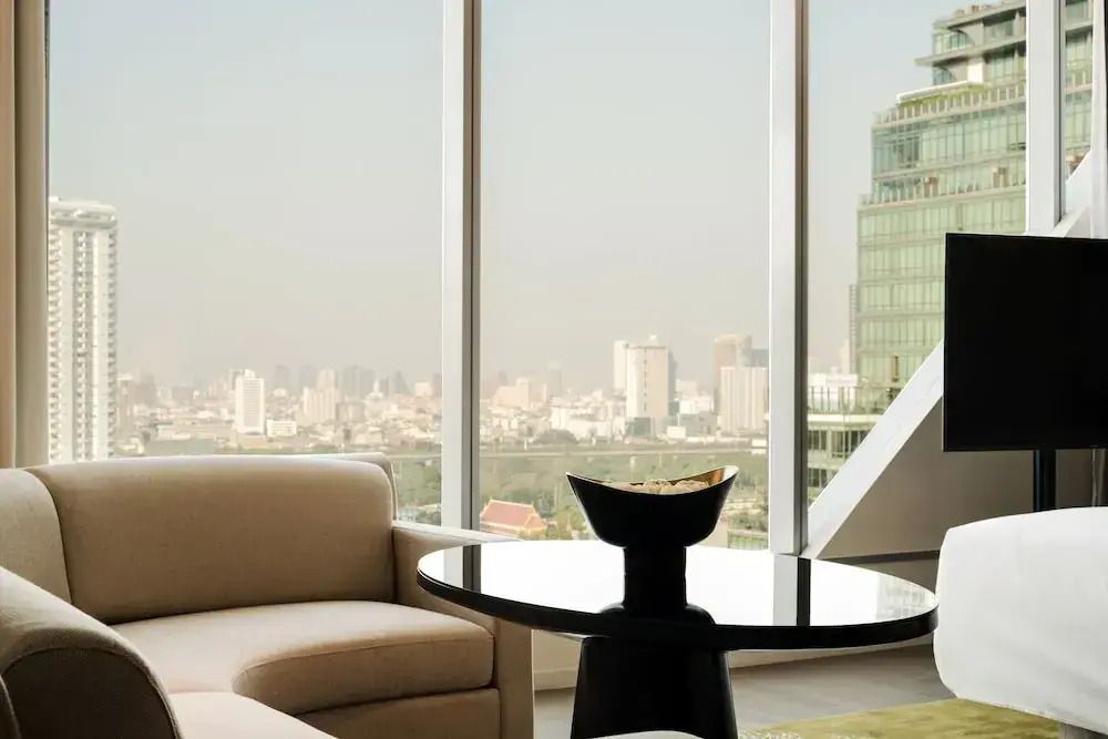 Wohnbereich des Deluxe Zimmers mit stilvollem Sofa und Blick auf Bangkok