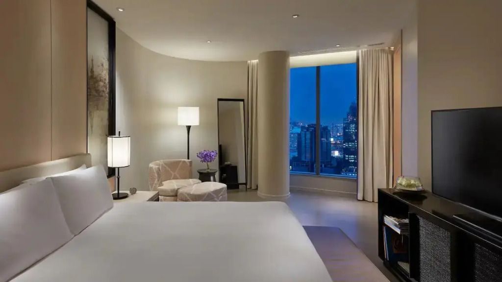 Geräumige Suite mit Doppelbett, Sessel, Blick auf die nächtliche Stadt