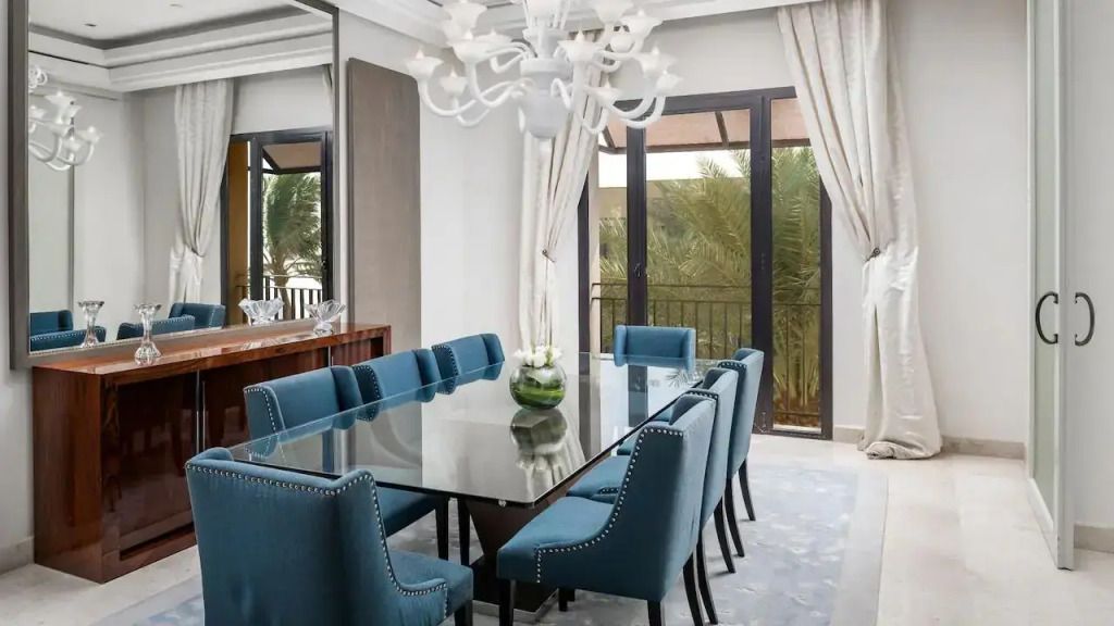 Esszimmer mit großem Glastisch und blauen Stühlen mit Balkonzugang