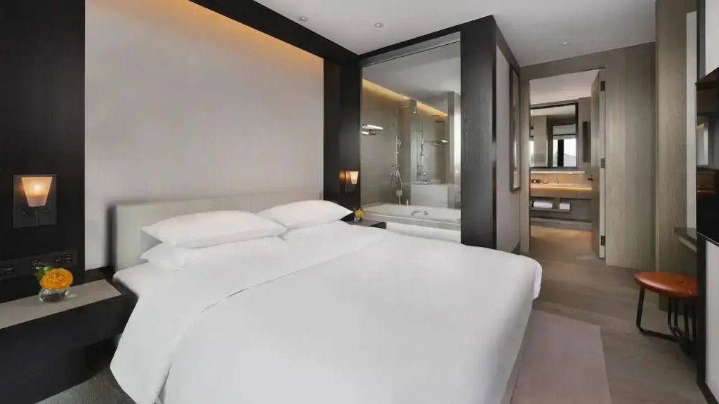 Elegantes Schlafzimmer mit weißem Doppelbett und großem Glaselement zum Bad
