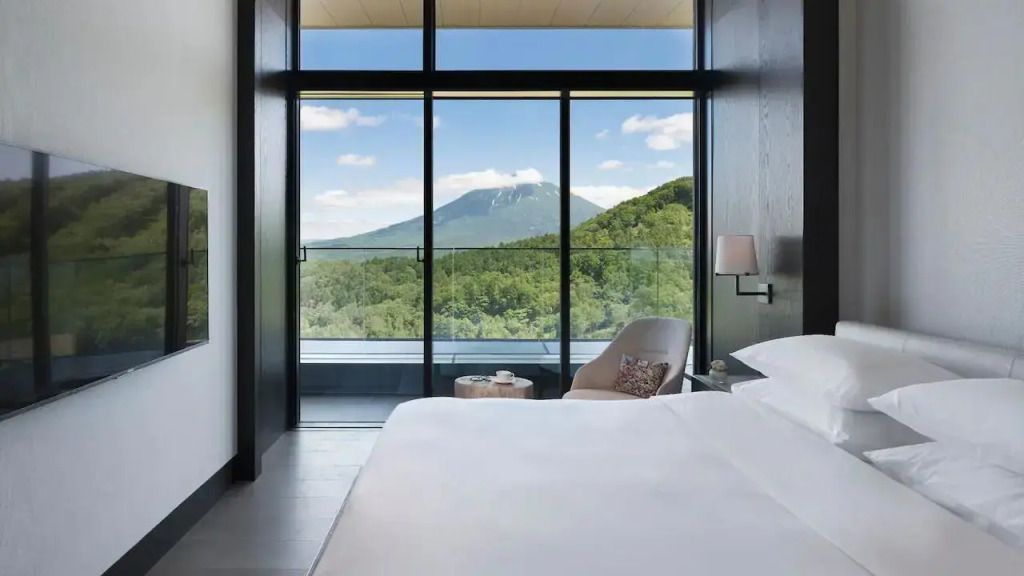 Helles Zimmer mit Panoramafenster und Blick auf bewaldete Berge unter klarem Himmel.