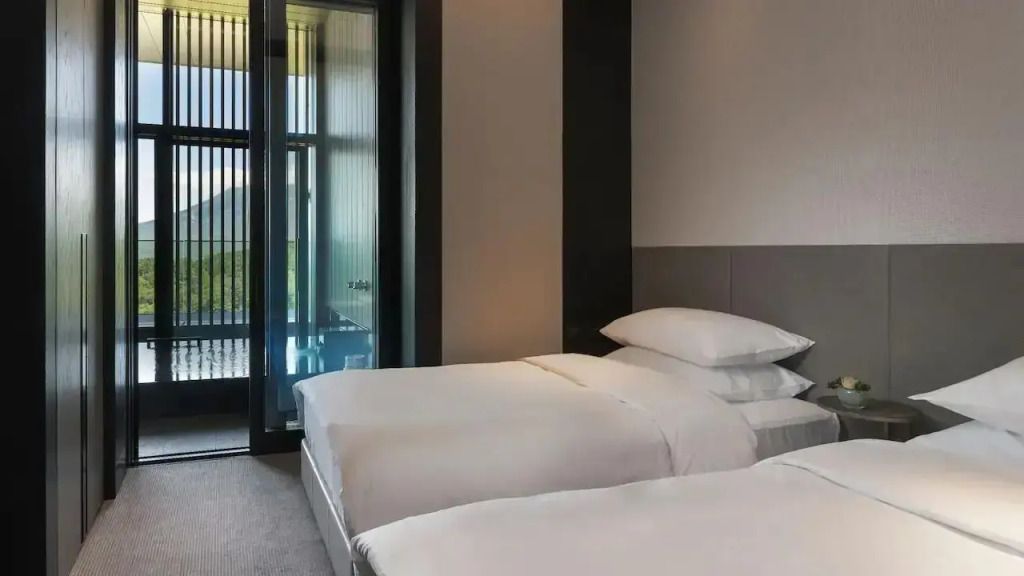 Modernes Doppelbettzimmer mit großer Fensterfront und sanfter Beleuchtung.