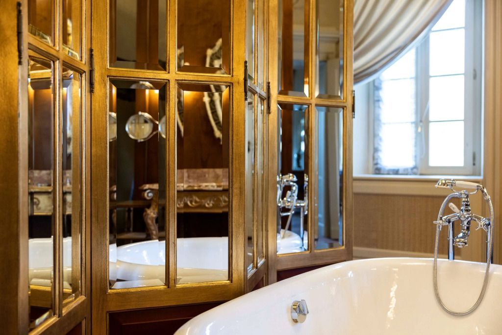 Elegante Badewanne mit goldenen Armaturen und großen Spiegeln in der Suite