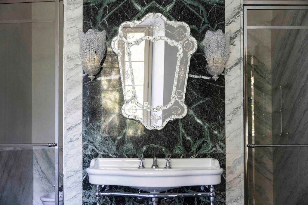 Luxuriöses Badezimmer mit kunstvollem Spiegel und Marmorwand.