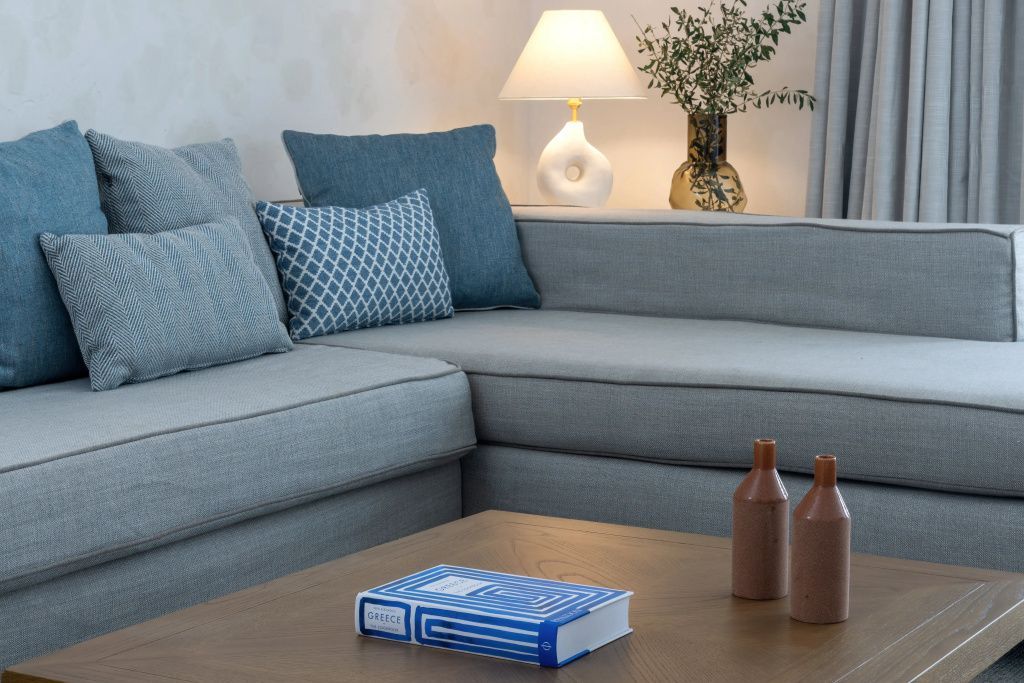 Gemütliche Sitzecke in einer Suite mit blauem Ecksofa, stilvoller Tischlampe und Holztisch.