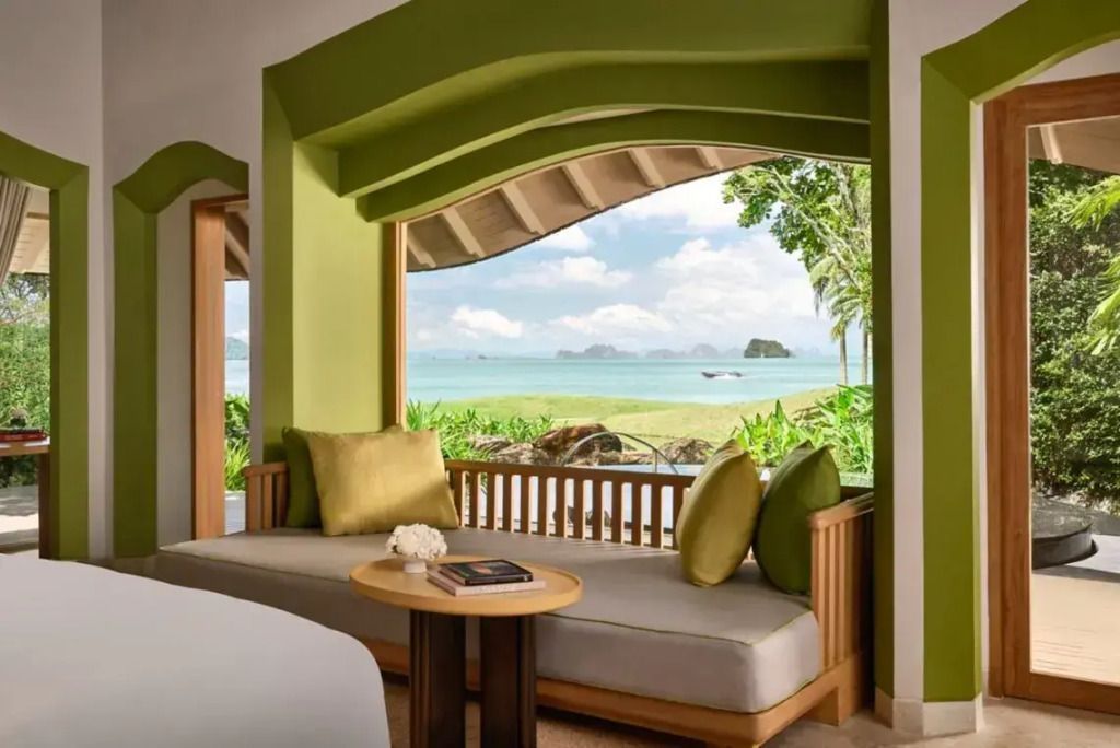 Großes Fenster mit Blick auf das Meer, ergänzt durch eine geräumige Sitzecke mit grünen Kissen.