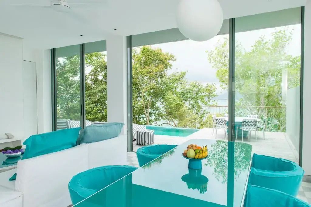 Moderne Lounge mit Glaswand und Poolblick umgeben von üppigem Grün