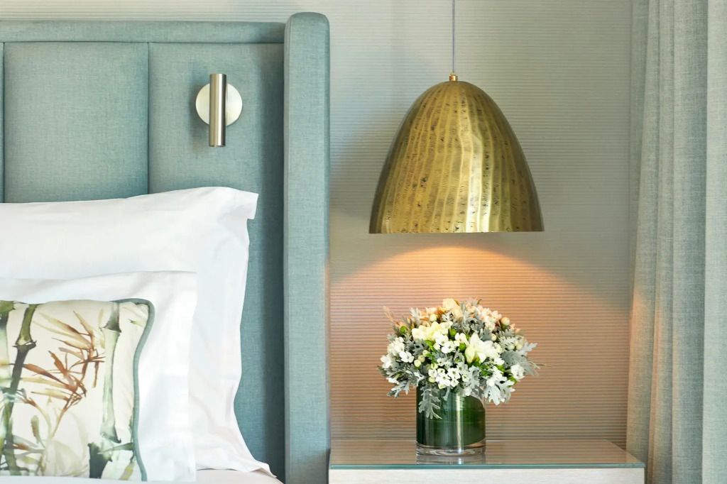 Nachttisch mit eleganter Lampe und Blumenarrangement, neben einem Bett.