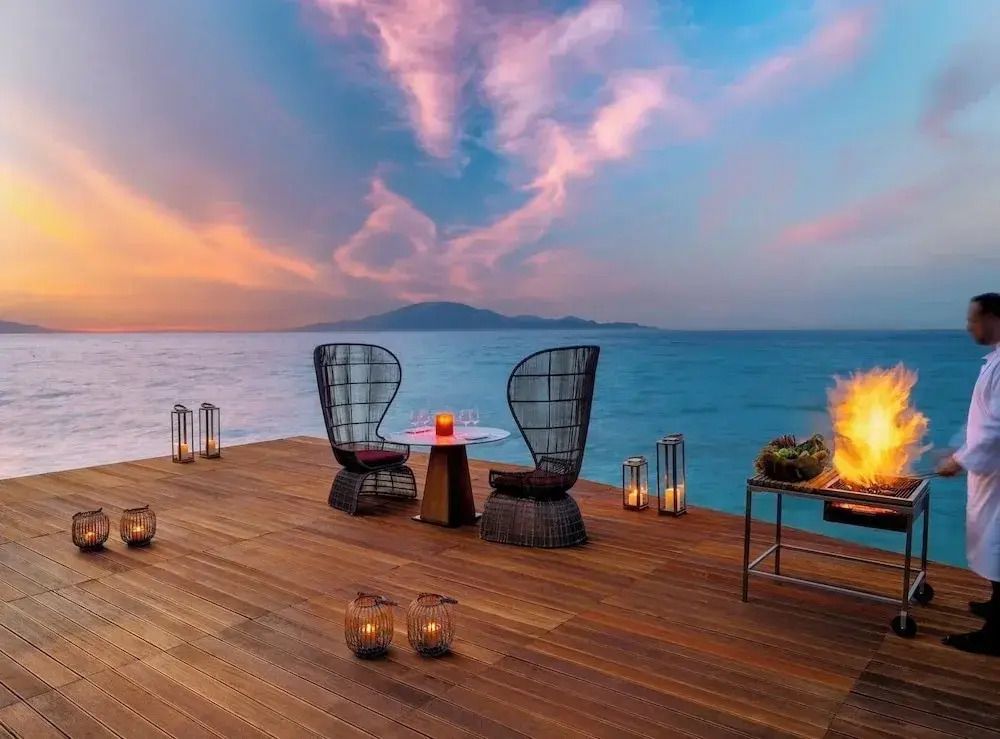 Romantischer Steg mit Sitzgelegenheiten und Dekoration am Meer bei Sonnenuntergang