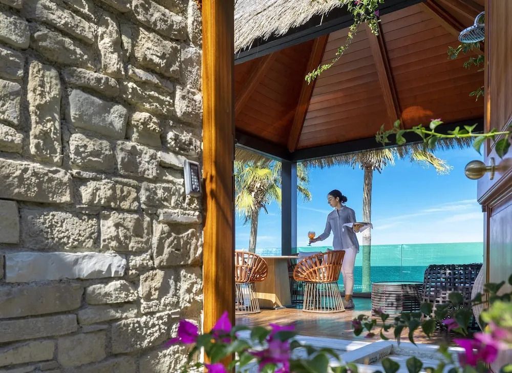Offener Lounge-Bereich mit Strohdach, Sitzgelegenheiten und Ausblick auf das Meer