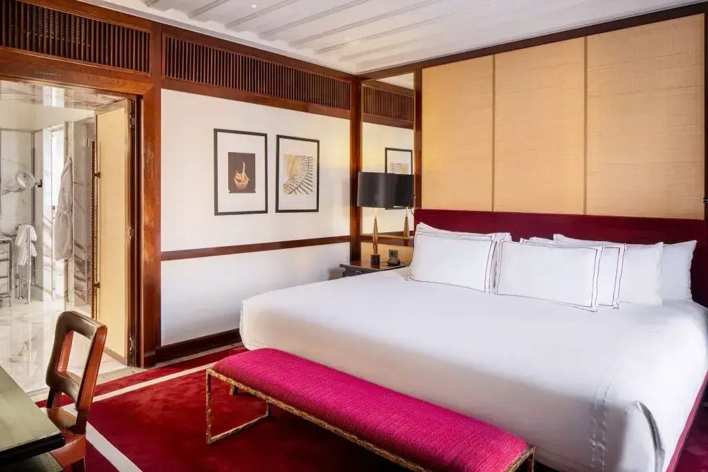 Elegantes Hotelzimmer mit großem Doppelbett, weißen Bettbezügen und rotem Teppich.