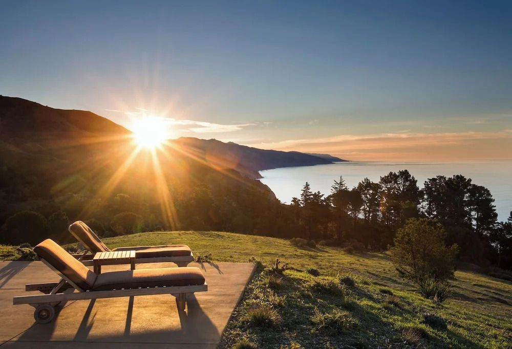 Sonnenuntergang über Hügeln und Ozean mit Liegestühlen im Vordergrund