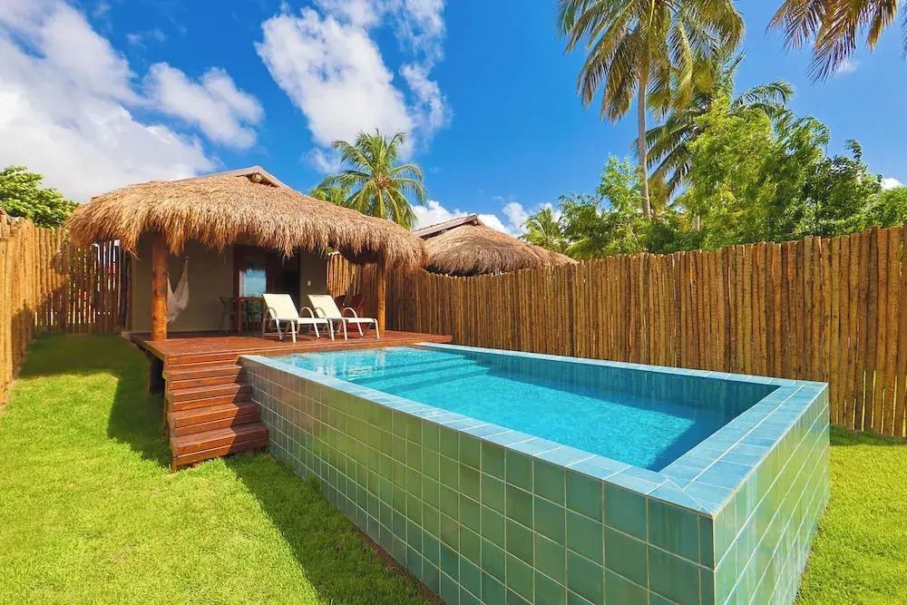 Modernes Bungalow mit Strohdach und privatem Pool umgeben von tropischen Pflanzen