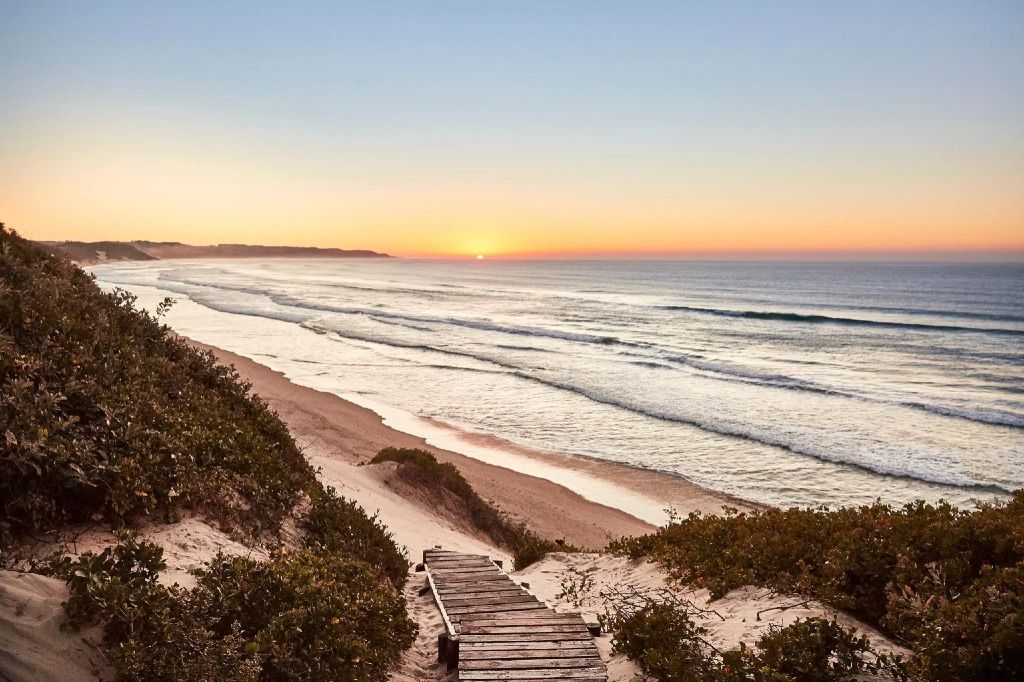 Malerischer Strand bei Sonnenuntergang mit Holzpfad durch Dünen