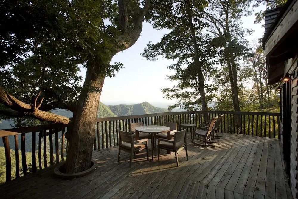 Große Holzterrasse mit Tisch und Stühlen neben einem Baum mit Blick auf die Berge