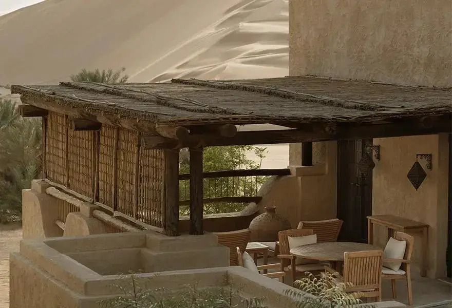 Terrasse mit Sitzgelegenheiten und traditioneller Architektur, Wüstensand im Hintergrund.