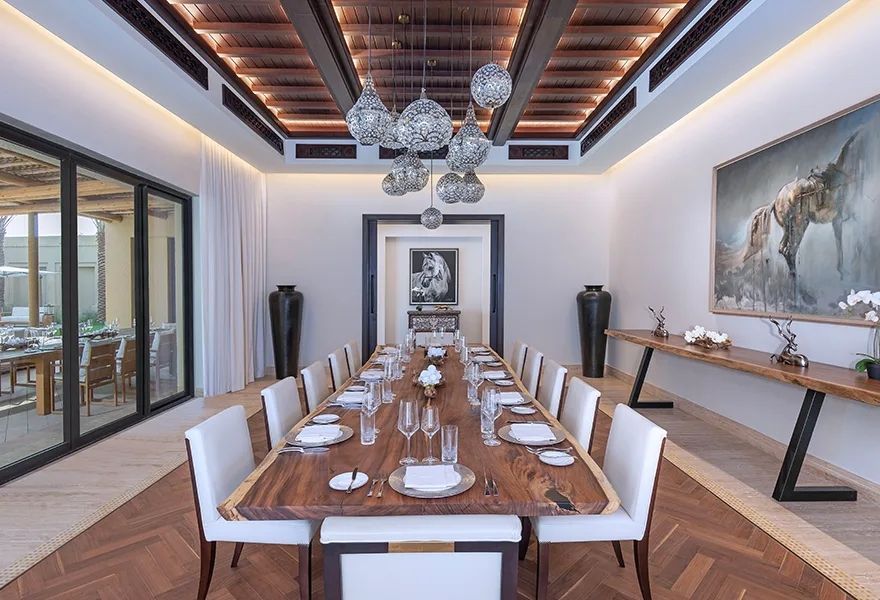 Eleganter Essbereich mit langem Holztisch und dezenter Beleuchtung im Wüstenresort.