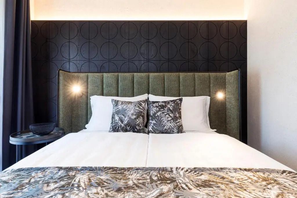 Gepolstertes Bett im luxuriösen Schlafzimmer mit kunstvollen Textilien und Beleuchtung.
