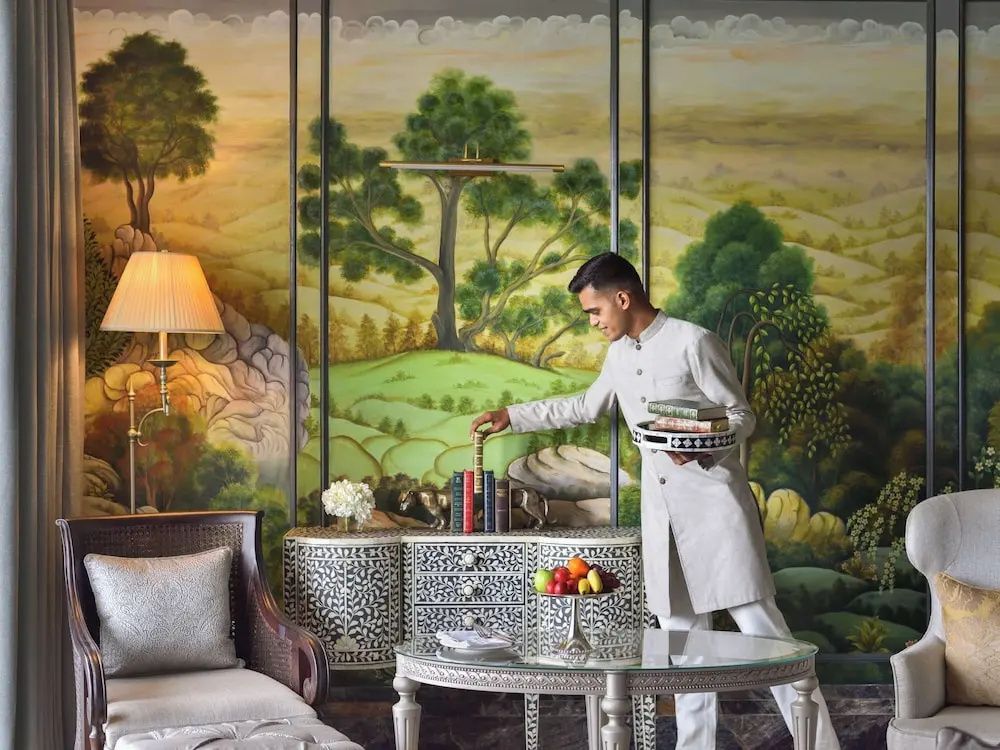 Butler in traditioneller Kleidung arrangiert Bücher in eleganter Suite.