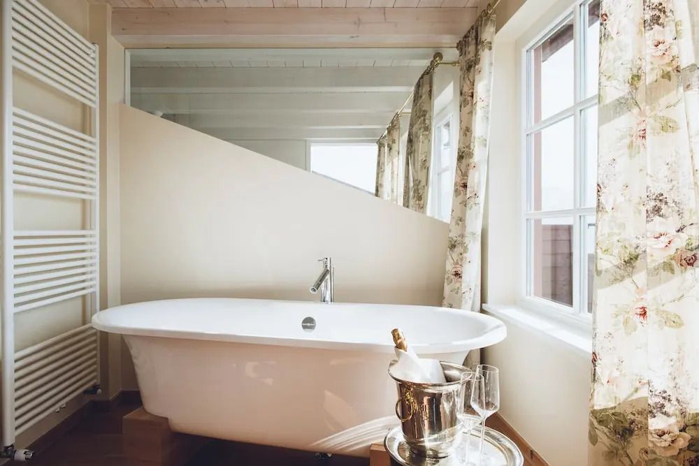 Freistehende Badewanne mit Champagner und Gläsern am Fenster