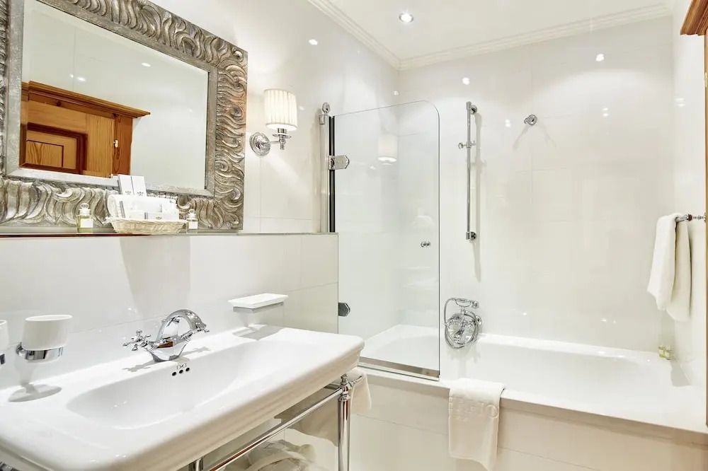 Weiß gefliestes Badezimmer mit eleganter Deko und Badewanne mit Duschwand.