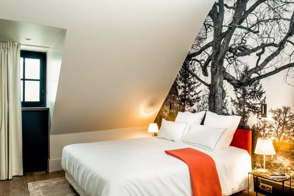 Gemütliches Doppelbett unter schrägem Dach mit Baumtapete.