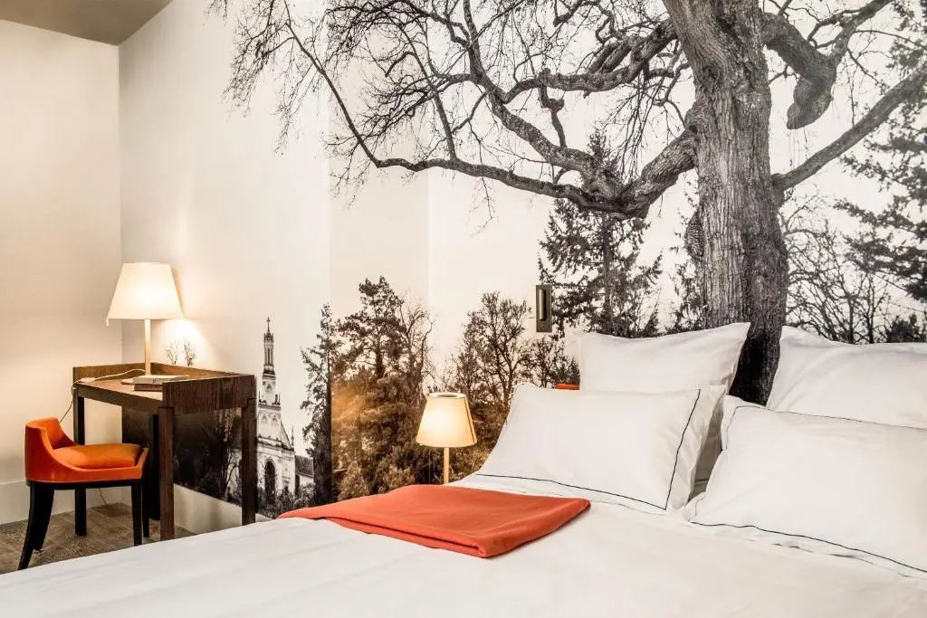Komfortables Bett mit Kunsttapete zeigt großen Baum über historischem Gebäude.