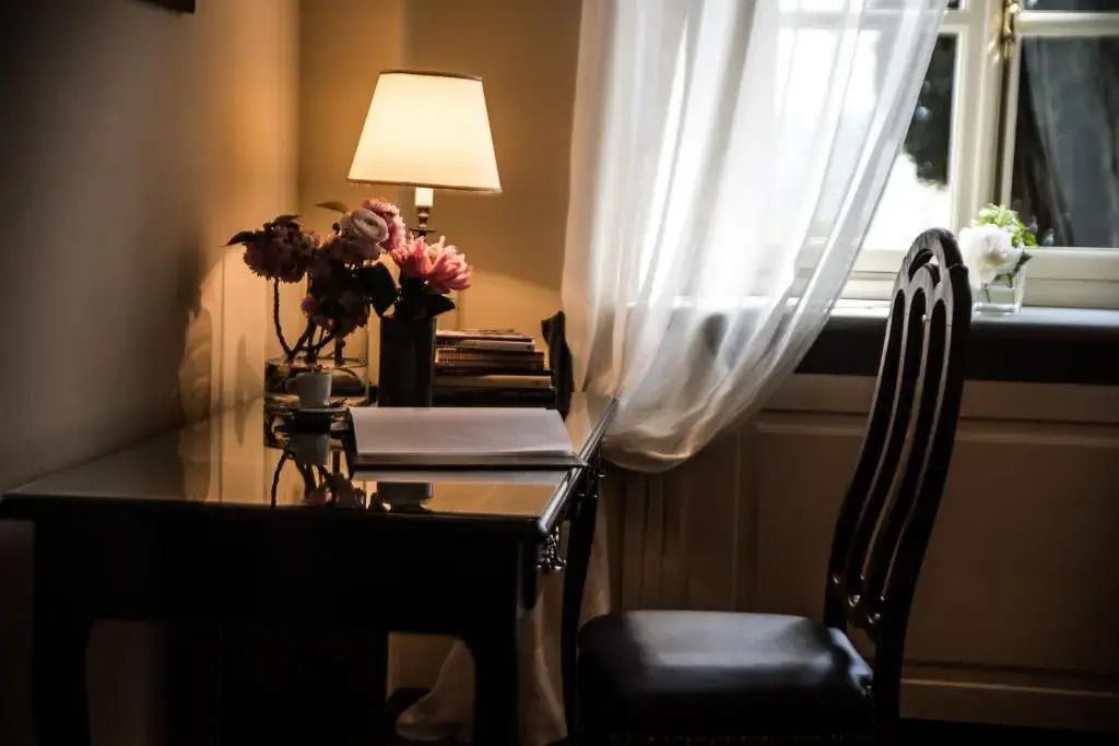Eleganter Schreibtischbereich mit Blumen und Lampe vor einem Fenster