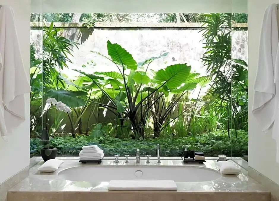 Luxuriöses Badezimmer mit Blick auf üppigen Garten und große Fenster
