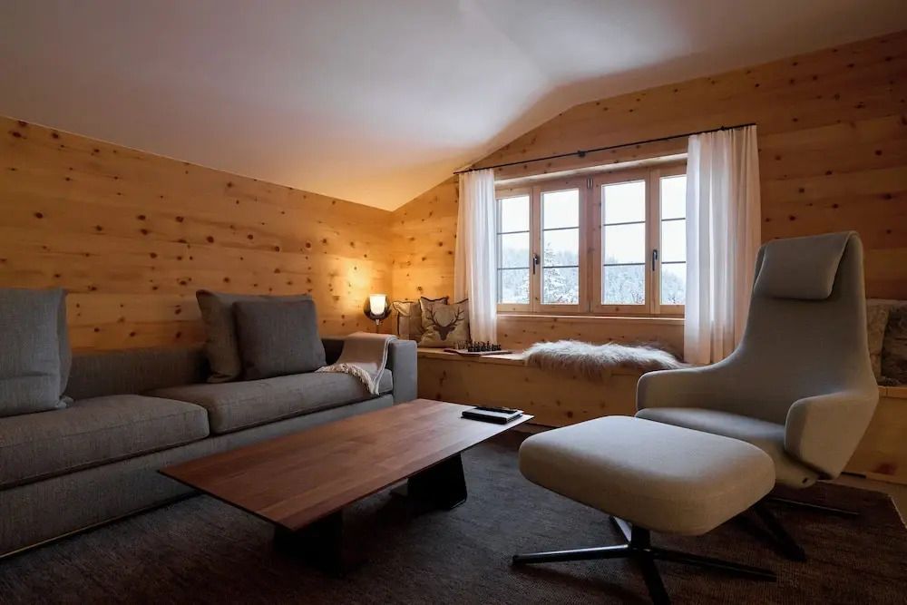 Gemütlicher Wohnzimmerbereich mit Holzwänden, Sofa, Sessel und großem Fenster.