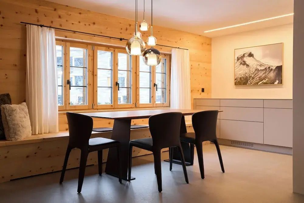 Essbereich mit Holzwänden, Esstisch und Designerstühlen unter eleganten Lampen.
