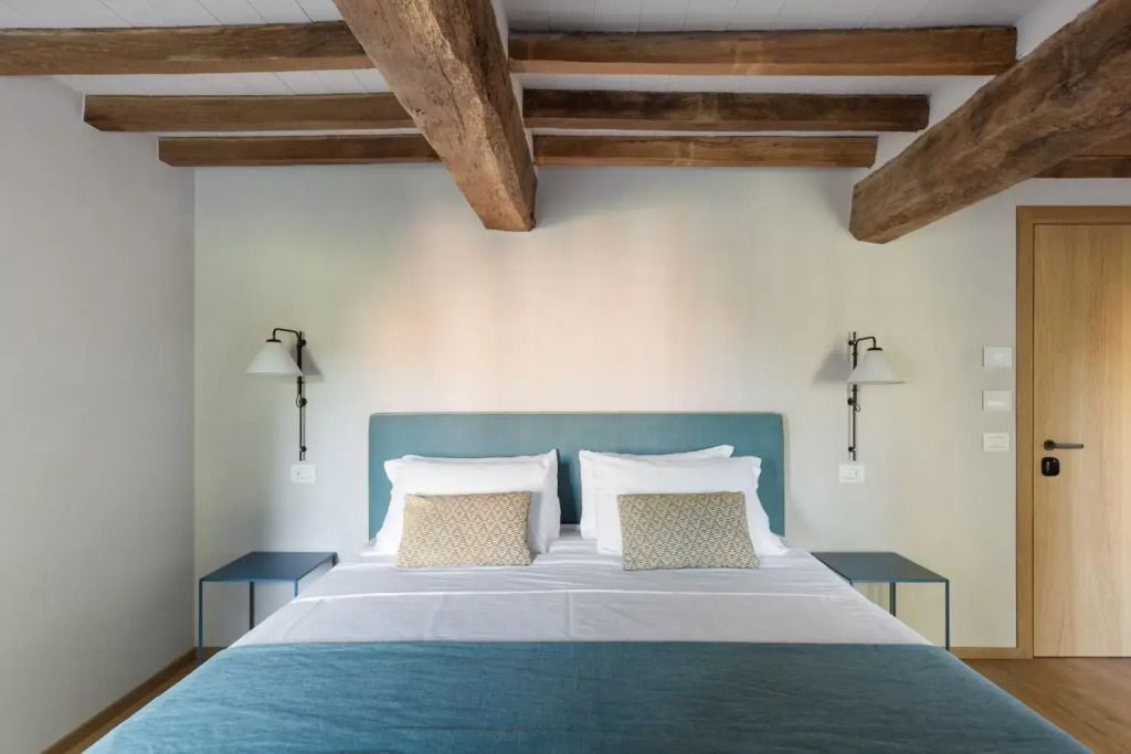 Komfortables Doppelbett mit Holzbalkendecke und eleganter Wandbeleuchtung