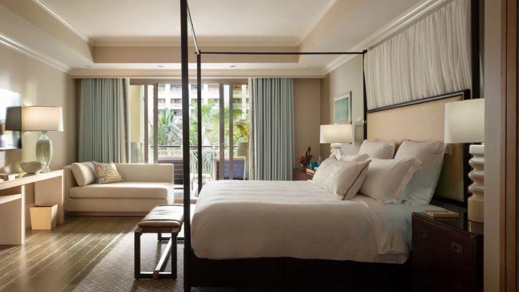 Helles Hotelzimmer mit Doppelbett, Sitzecke und Balkonaussicht auf den Garten.