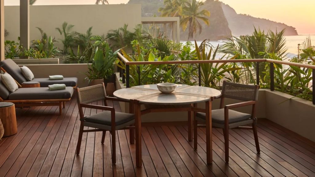 Holzterrasse mit Rundtisch, Stühlen und üppiger Vegetation am Meer