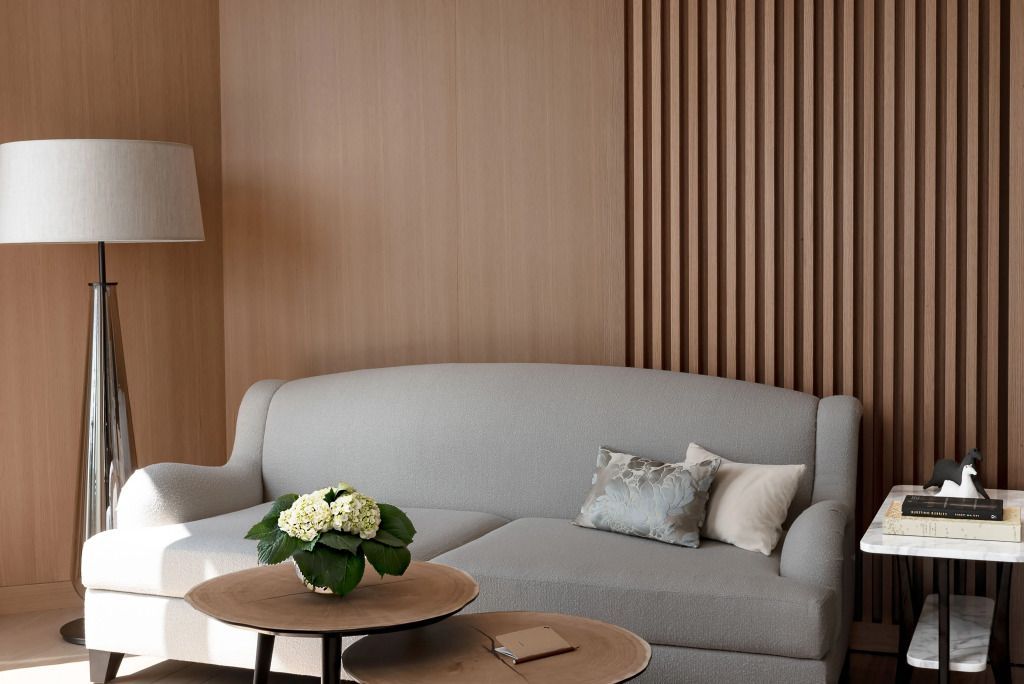 Graues Sofa mit stilvollen Kissen, Holzwand und einem runden Kaffeetisch mit Dekoration