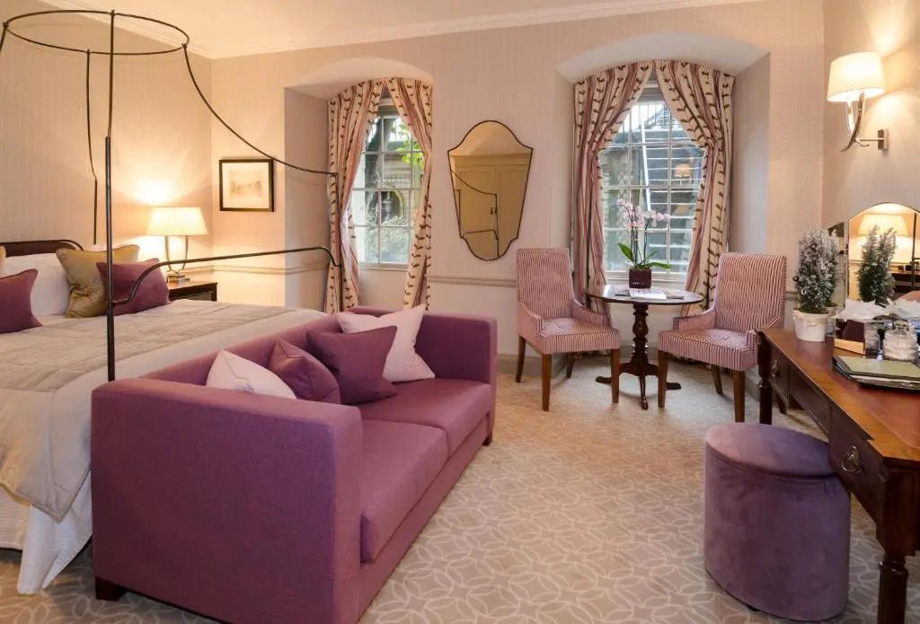 Stilvoll eingerichtetes Schlafzimmer mit lila Sofa und großen Fenstern