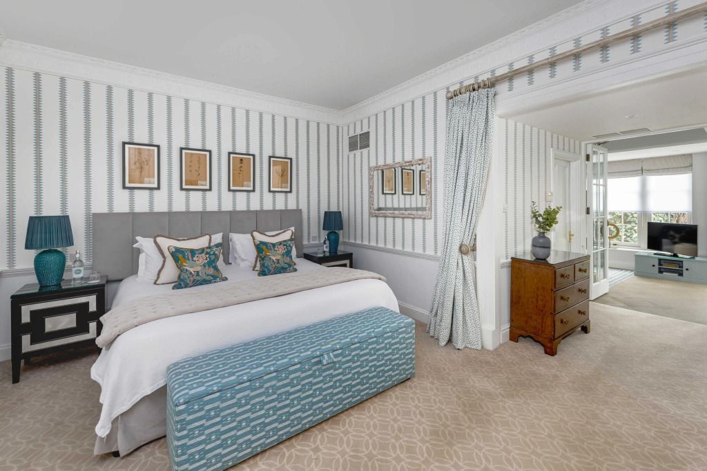 Elegantes Schlafzimmer mit großem Bett, blauer Bank und stilvoller Tapete