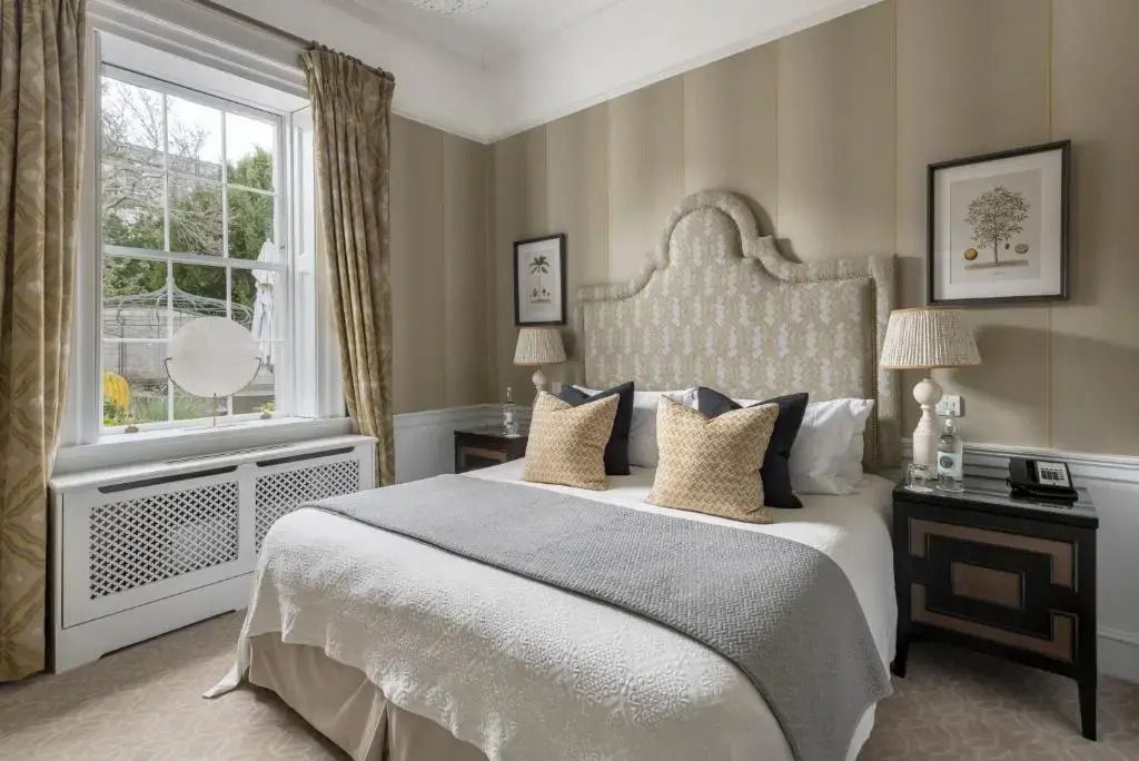 Luxuriöses Schlafzimmer mit großem Bett, dekorativem Kopfteil und Fenster mit Blick auf Garten