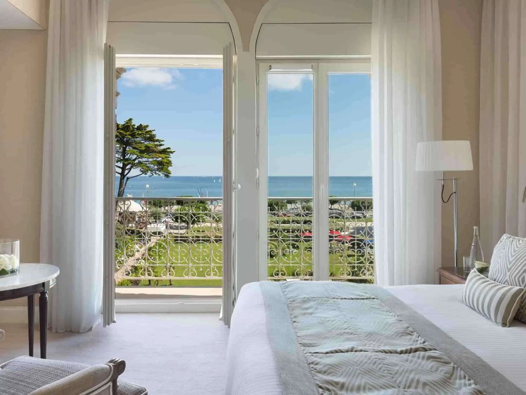 Elegantes Zimmer mit Doppelbett und Meerblick durch große Fenster.