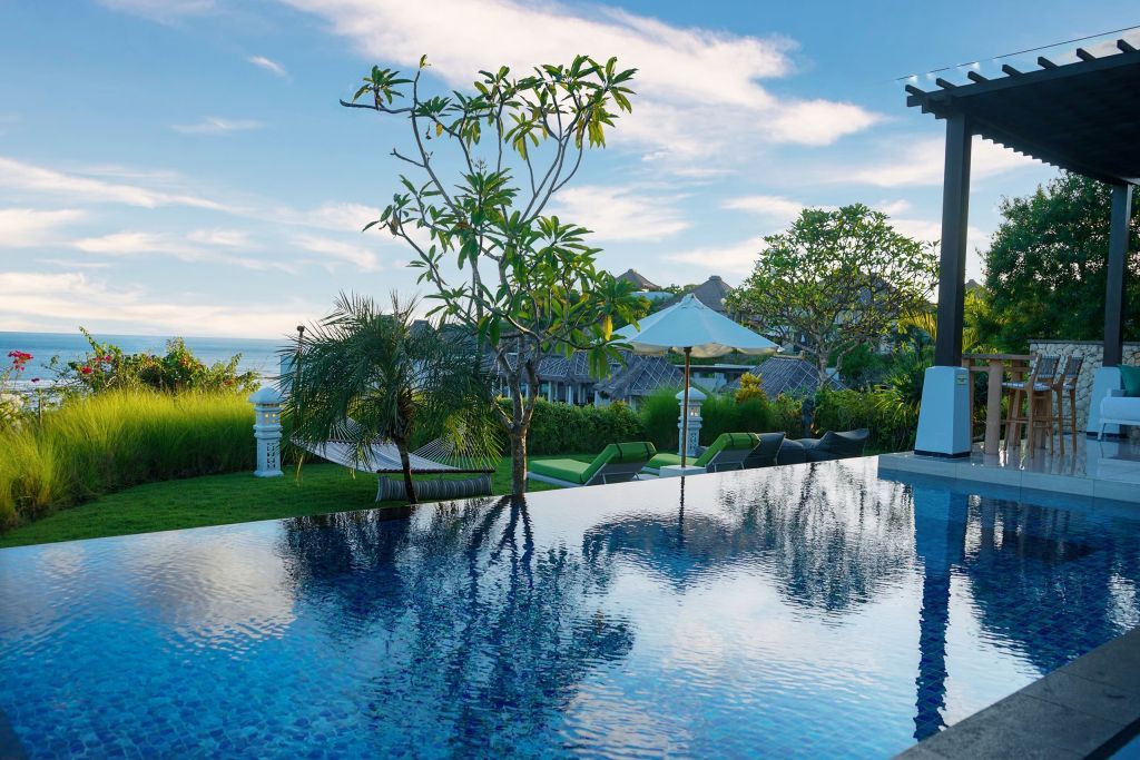 Infinity Pool mit Blick auf Garten und Meer bei Sonnenuntergang