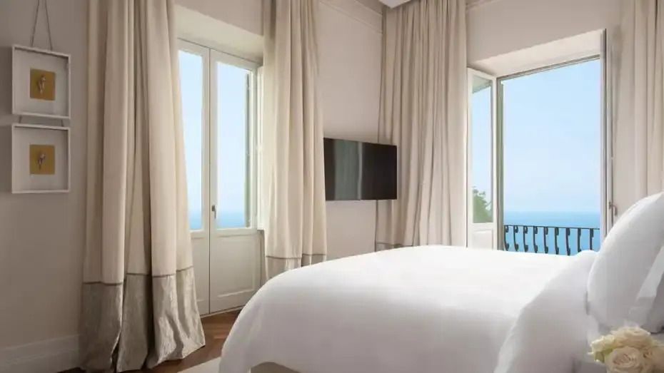 Helles Schlafzimmer mit Doppelbett und Blick auf das Meer aus geöffneten Fenstern.