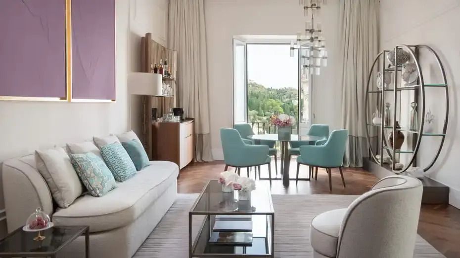 Wohnzimmer mit eleganter Sofagarnitur, blaugrünen Sesseln und Blick auf die Natur durch Fenster.