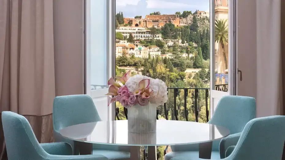 Blumendekoration auf einem Tisch vor einem Fenster, das auf eine malerische Landschaft blickt.