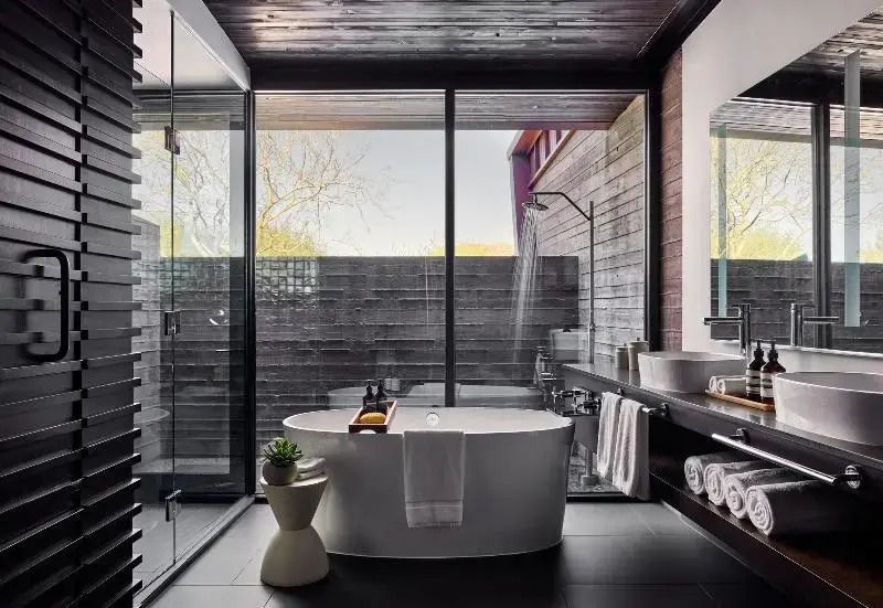 Luxuriöses Badezimmer mit freistehender Badewanne und Glasdusche mit Gartenblick.